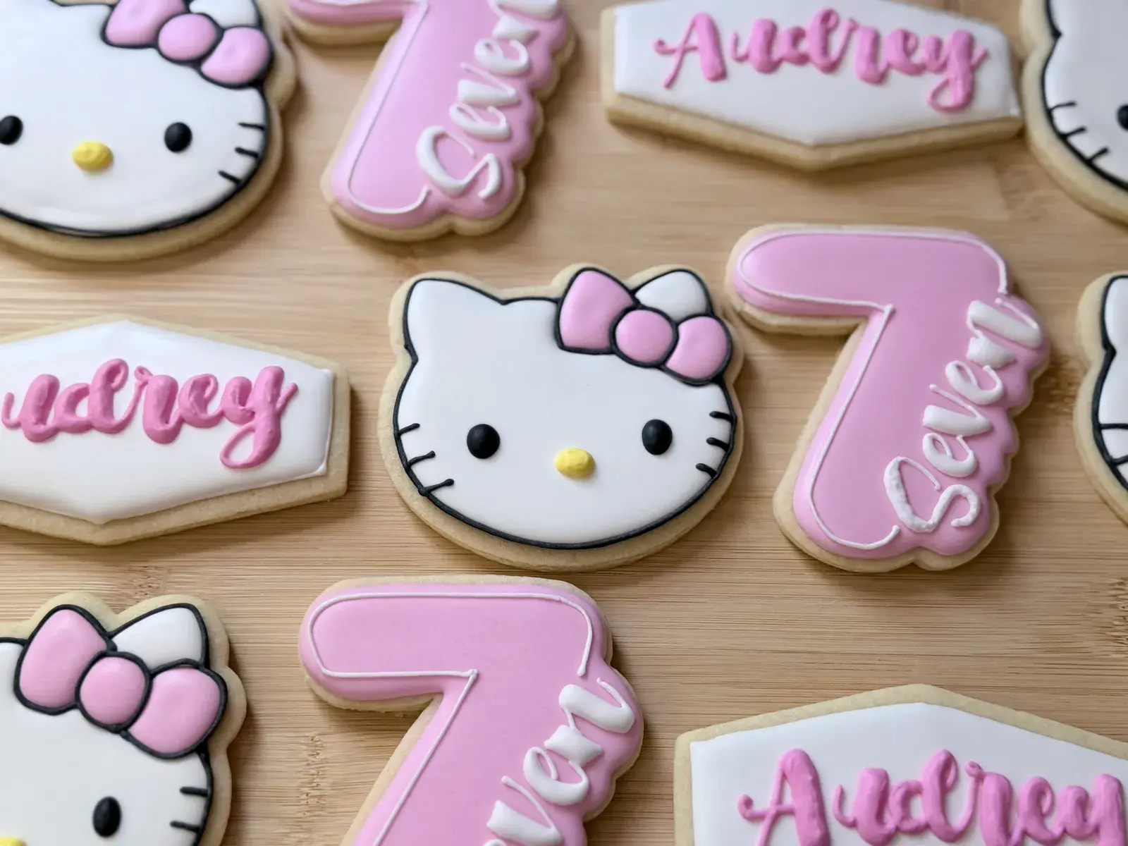 Hello Kitty birthday cookies in pink and white, including a Hello Kitty face with a bow, the name Audrey in pink script, and numeral 7 or Seven cookies marking a seventh birthday.