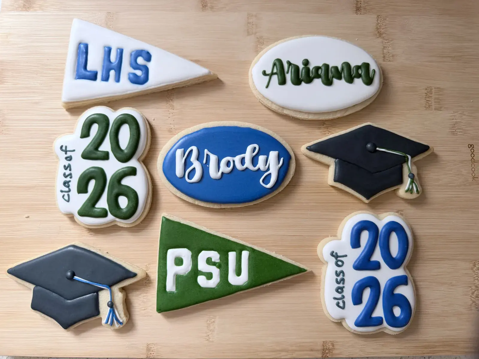 The same graduation cookie set from a closer angle, showing the Ariana name cookie, a graduation cap with tassel, and a blue Class of 2026 plaque on a wood board.